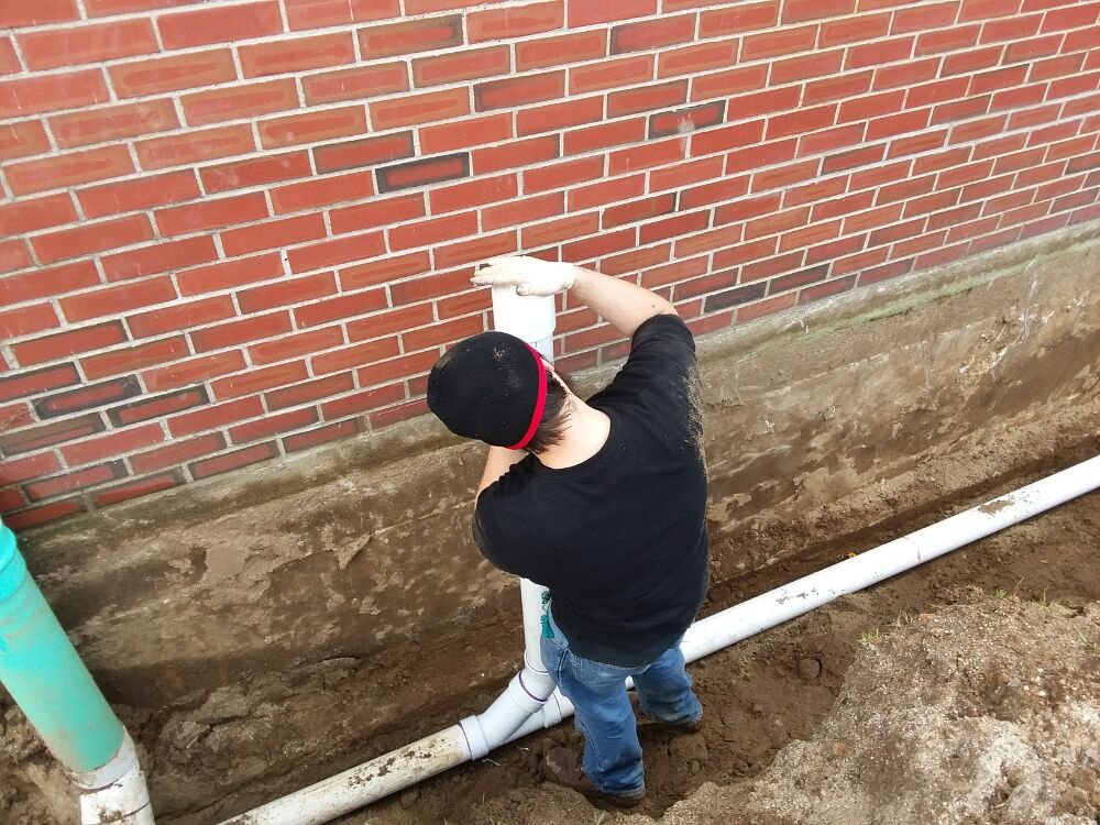 Technician assembling a new PVC pipe riser against a foundation wall